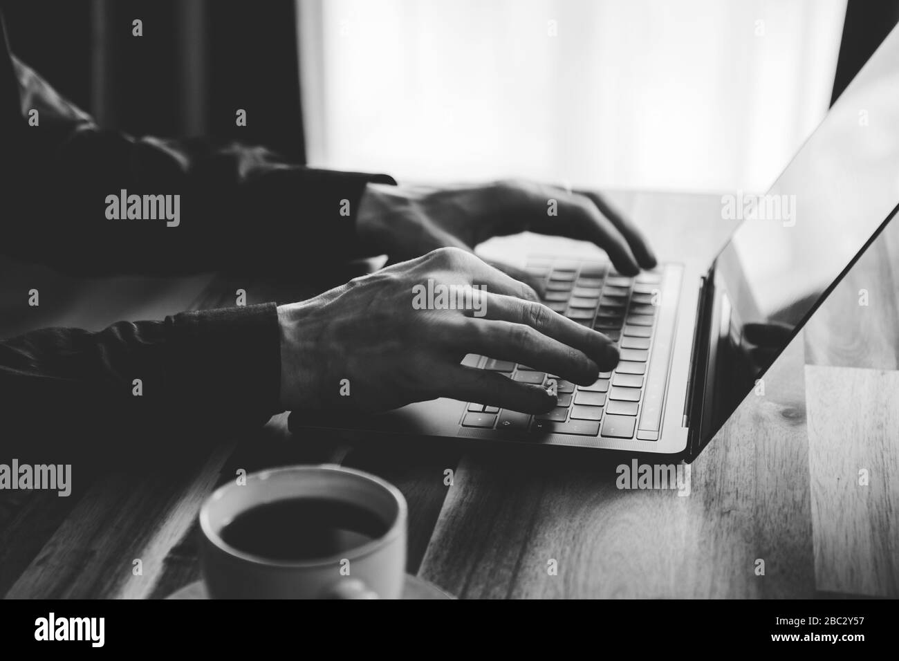 Un homme est en train de taper sur un clavier d'ordinateur portable. Concept de travail à domicile, photo en noir et blanc. Banque D'Images