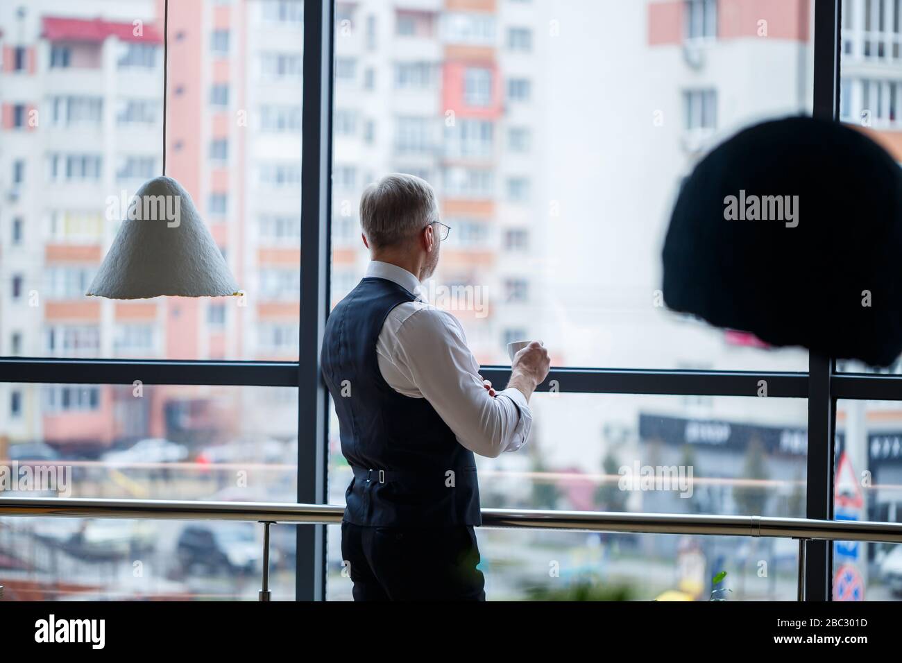 Sourire heureux directeur général pense à son développement de carrière réussi tout en se tenant avec une tasse de café dans sa main dans son bureau près de la Banque D'Images