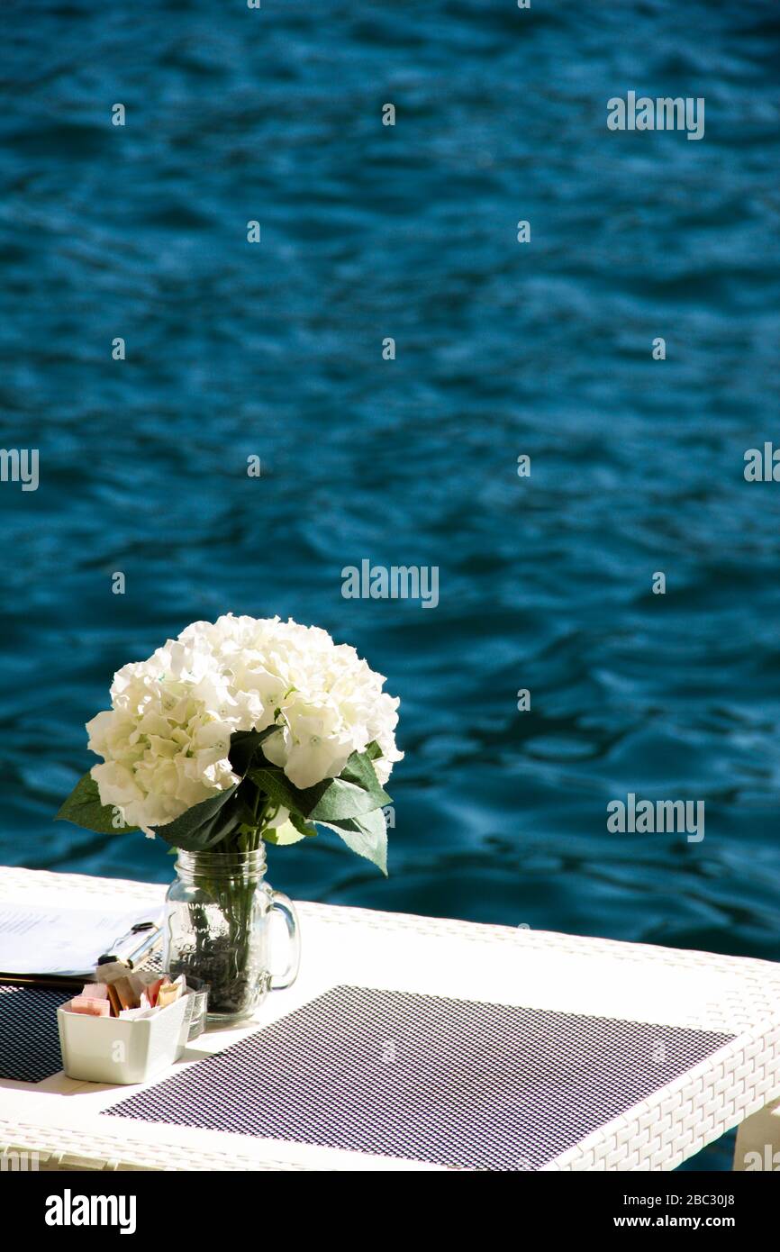 Bel endroit pour dîner au bord de la mer avec des fleurs blanches. Table en bordure de rive prête pour les nouveaux clients. Beaucoup d'espace-copie Banque D'Images