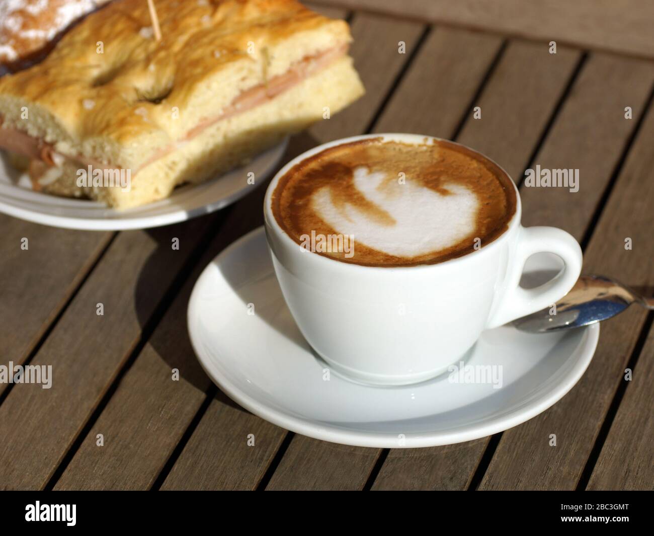 Merveilleux petit déjeuner italien traditionnel dans un café en plein air. Délicieux cappuccino italien chaud dans une tasse avec une soucoupe sur une table en bois. Banque D'Images
