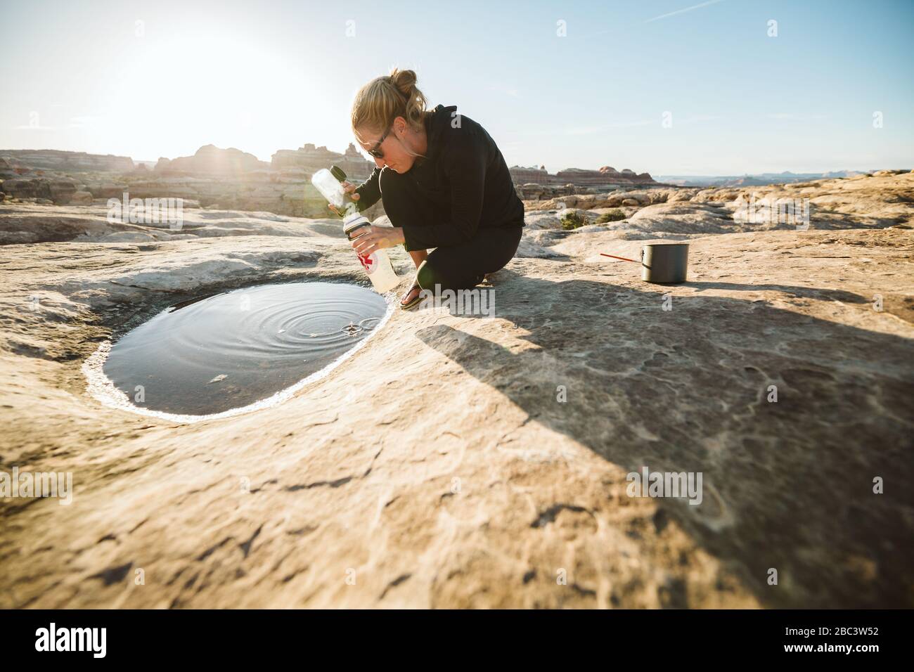 la camper féminine recueille l'eau pour la cuisson à partir d'une flaque peu profonde Banque D'Images