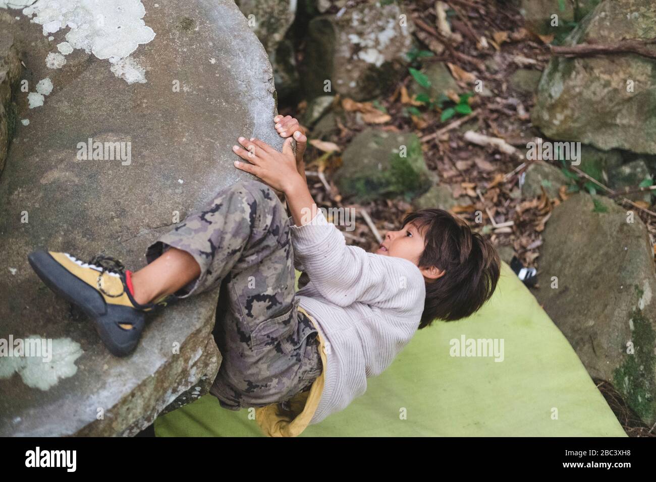 Petit garçon grimpant un rocher à l'extérieur Banque D'Images