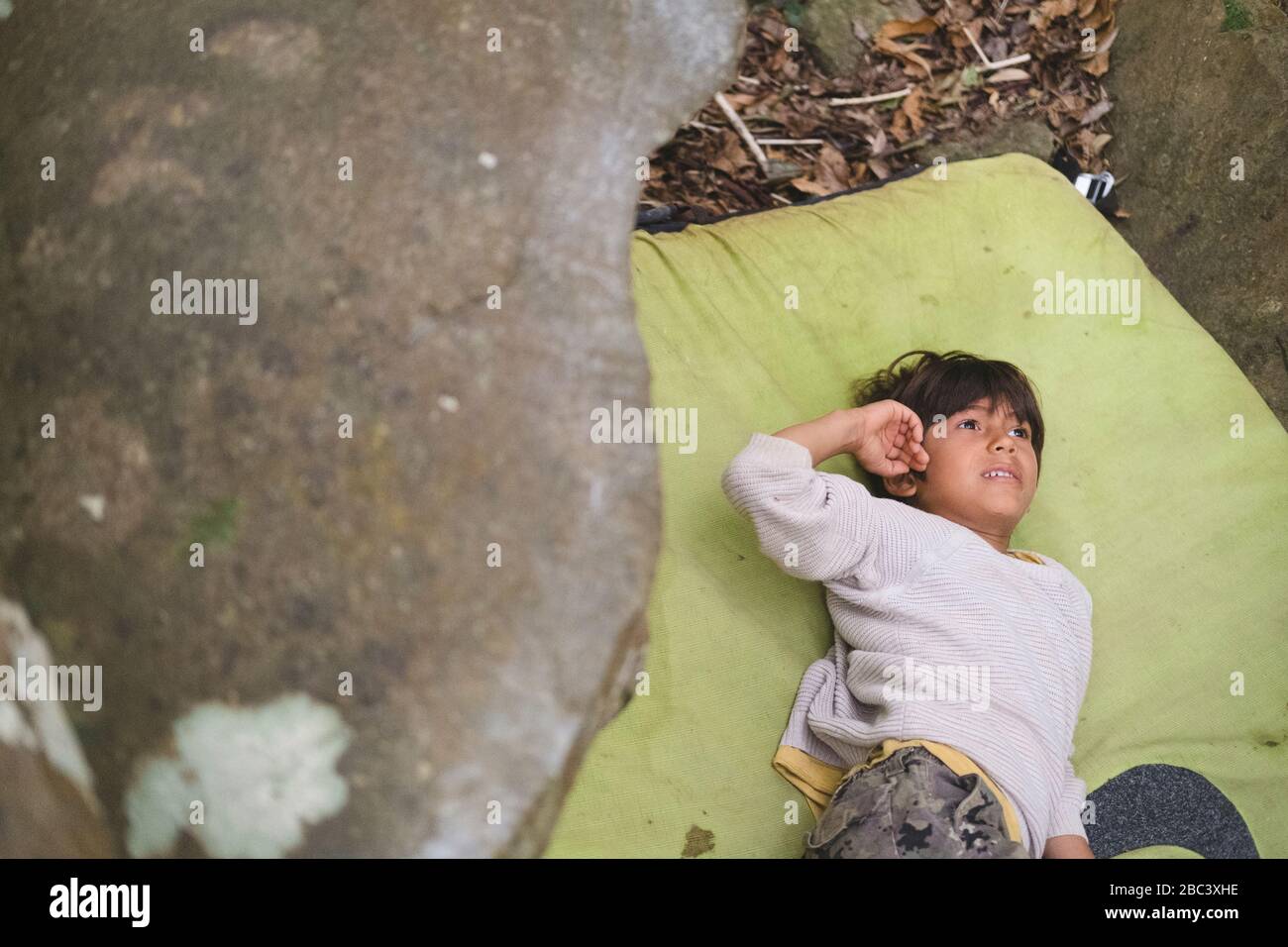 Le petit garçon repose sur un pataillage à côté d'un rocher Banque D'Images