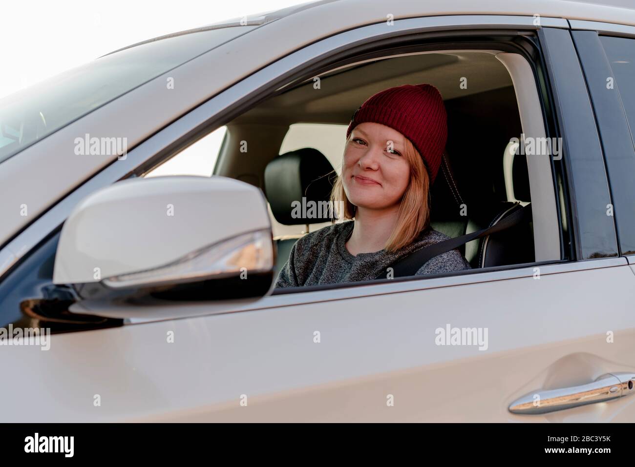 Femme souriant à l'appareil photo depuis la voiture au coucher du soleil Banque D'Images