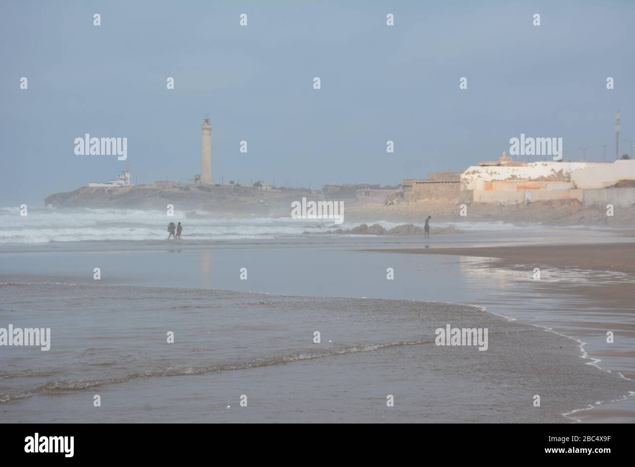 Les habitants de la région se baignent et jouent dans la mer sur la plage publique de Casablanca, au Maroc, avec le phare historique El Hank en arrière-plan. Banque D'Images