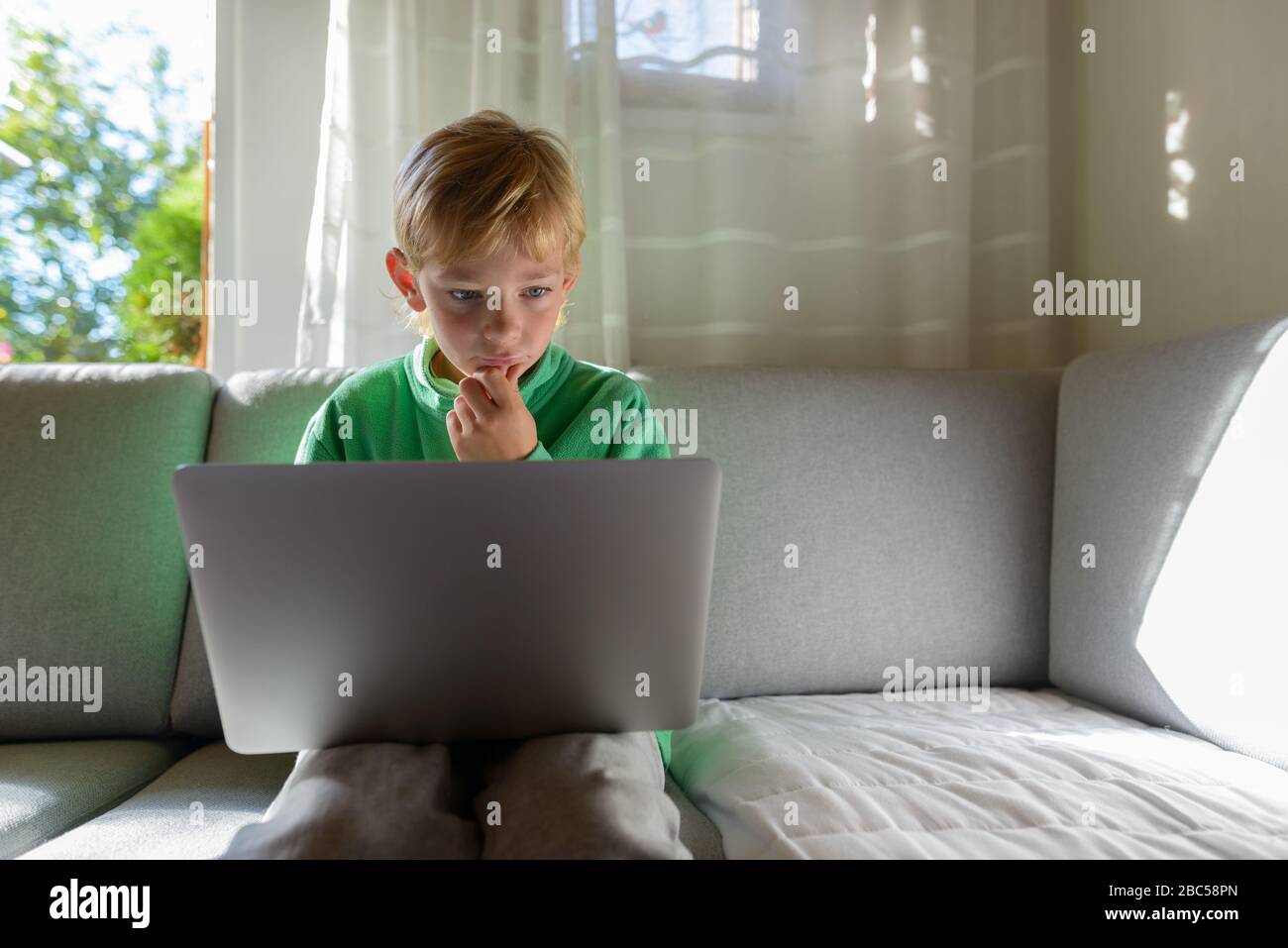 Jeune beau garçon pensant tout en utilisant l'ordinateur portable sur le canapé à la maison Banque D'Images
