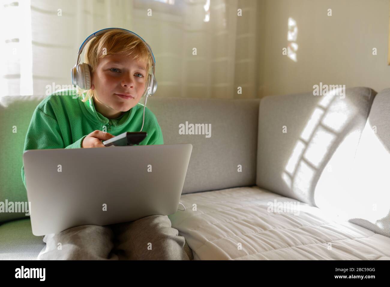 Jeune beau garçon avec casque et ordinateur portable regardant la télévision à la maison Banque D'Images