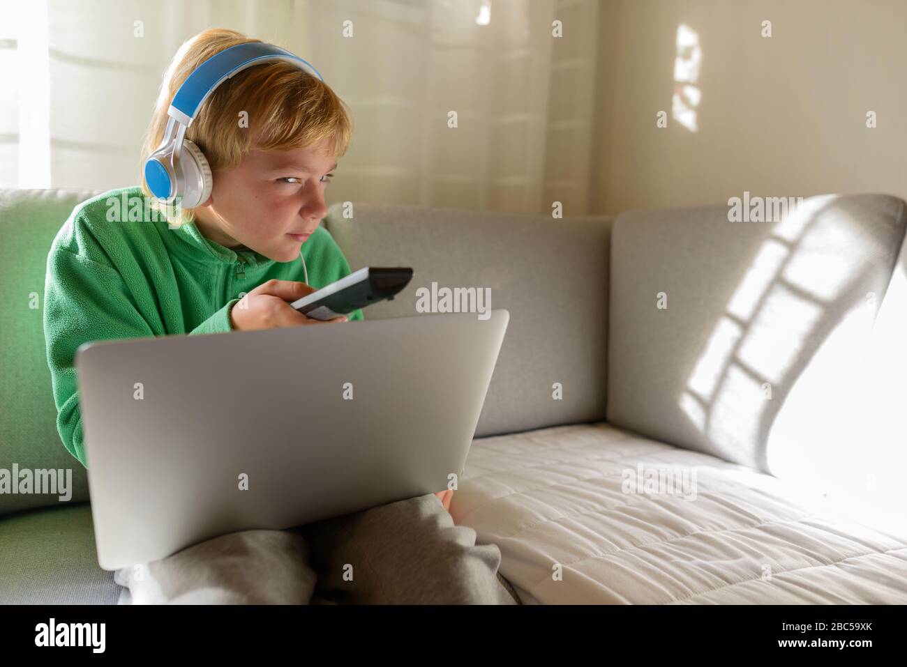 Jeune garçon avec casque et ordinateur portable semble douteux en regardant la télévision à la maison Banque D'Images