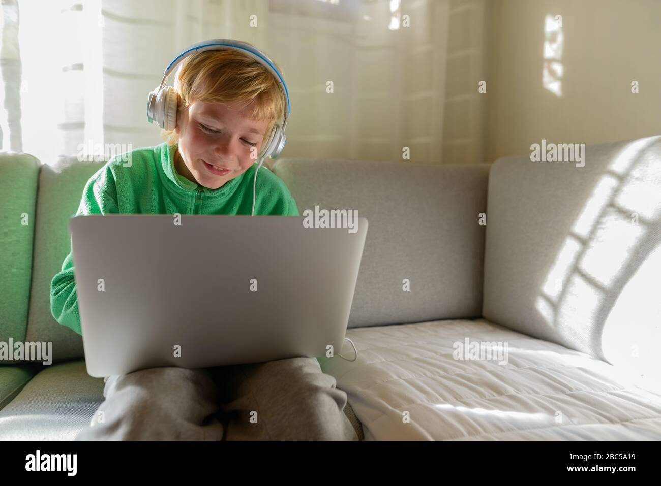 Joyeux jeune garçon avec casque utilisant un ordinateur portable à la maison Banque D'Images