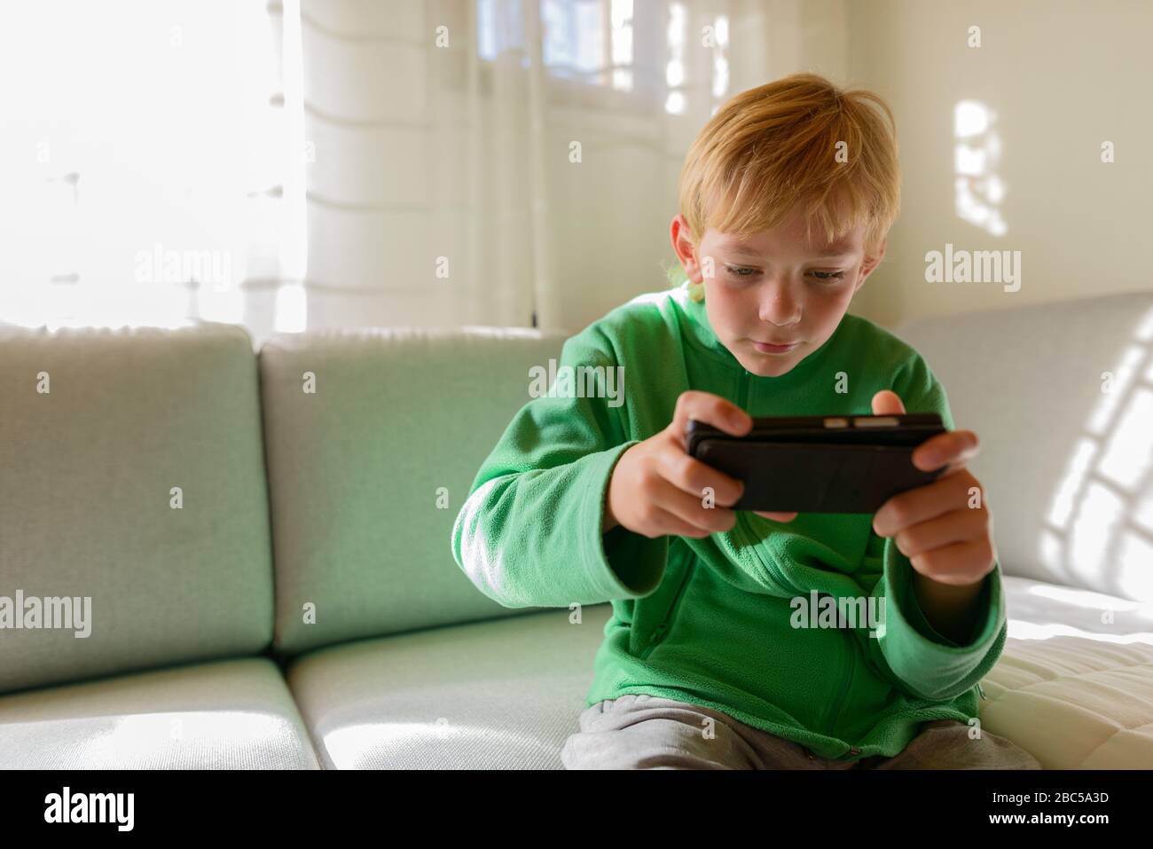 Jeune beau garçon utilisant le téléphone sur le canapé à la maison Banque D'Images