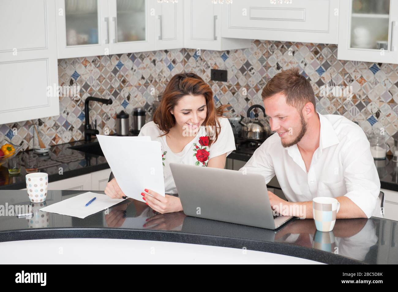 jeune homme de famille et femme assis avec des papiers et un ordinateur portable dans la cuisine pendant la quarantaine auto-isolation Banque D'Images