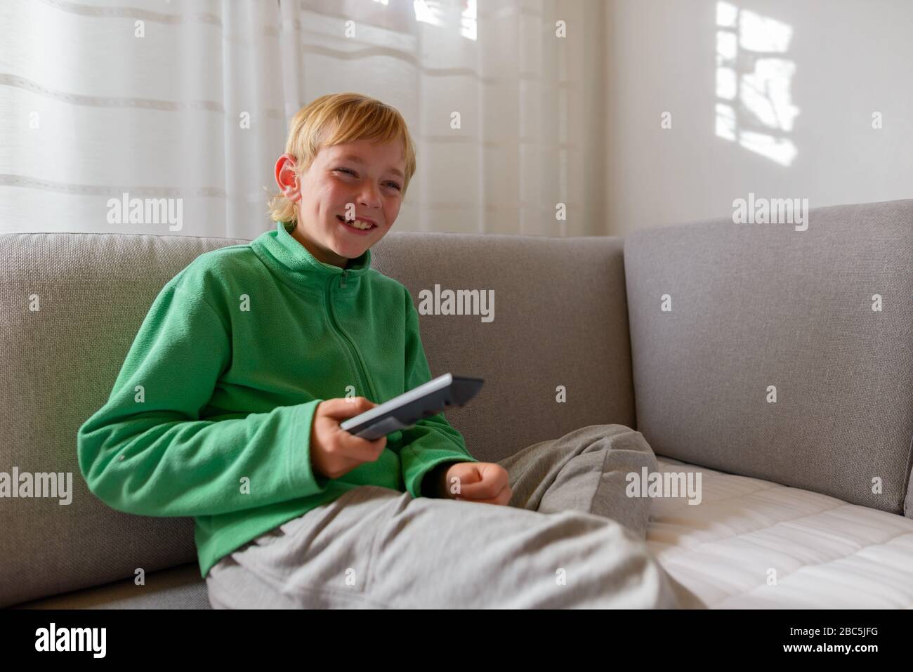 Joyeux jeune beau garçon regardant la télévision sur le canapé à la maison Banque D'Images