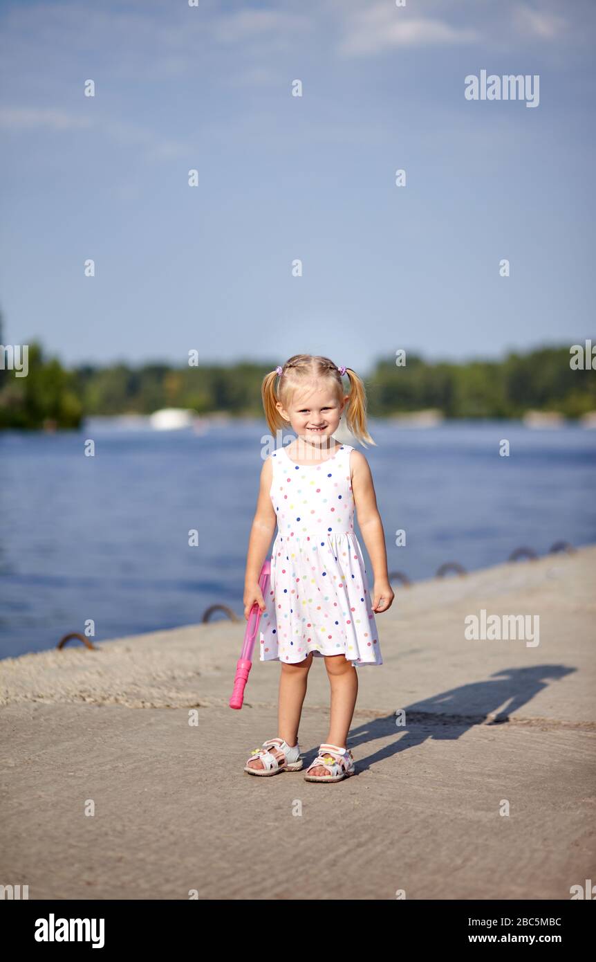 Adorable enfant en robe blanche posant à l'extérieur.Fille s'amuser. Petite fille de bébé dans le parc Banque D'Images