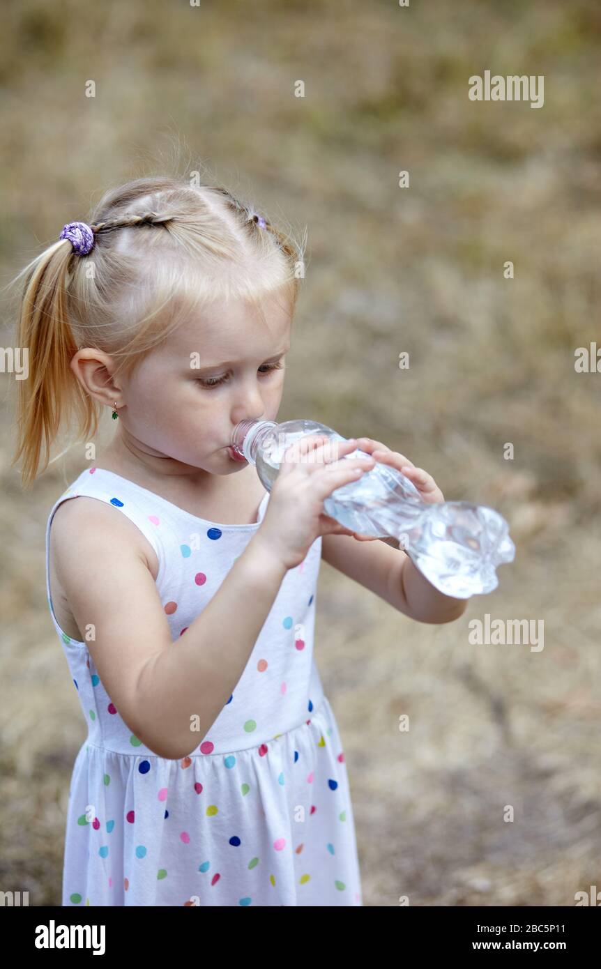 Une petite fille boit de l'eau à partir d'une bouteille dans le parc Banque D'Images
