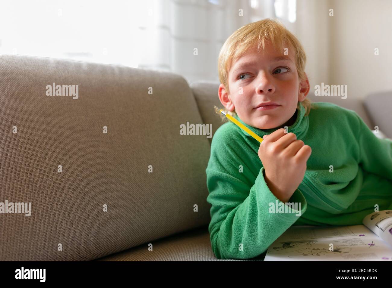 Jeune beau garçon pensant tout en étudiant sur le canapé à la maison Banque D'Images
