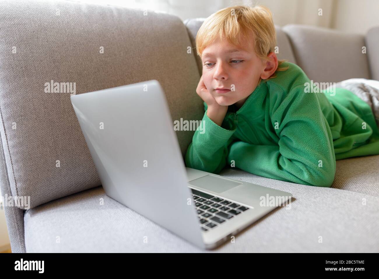 Jeune beau garçon pensant tout en utilisant l'ordinateur portable sur le canapé à la maison Banque D'Images