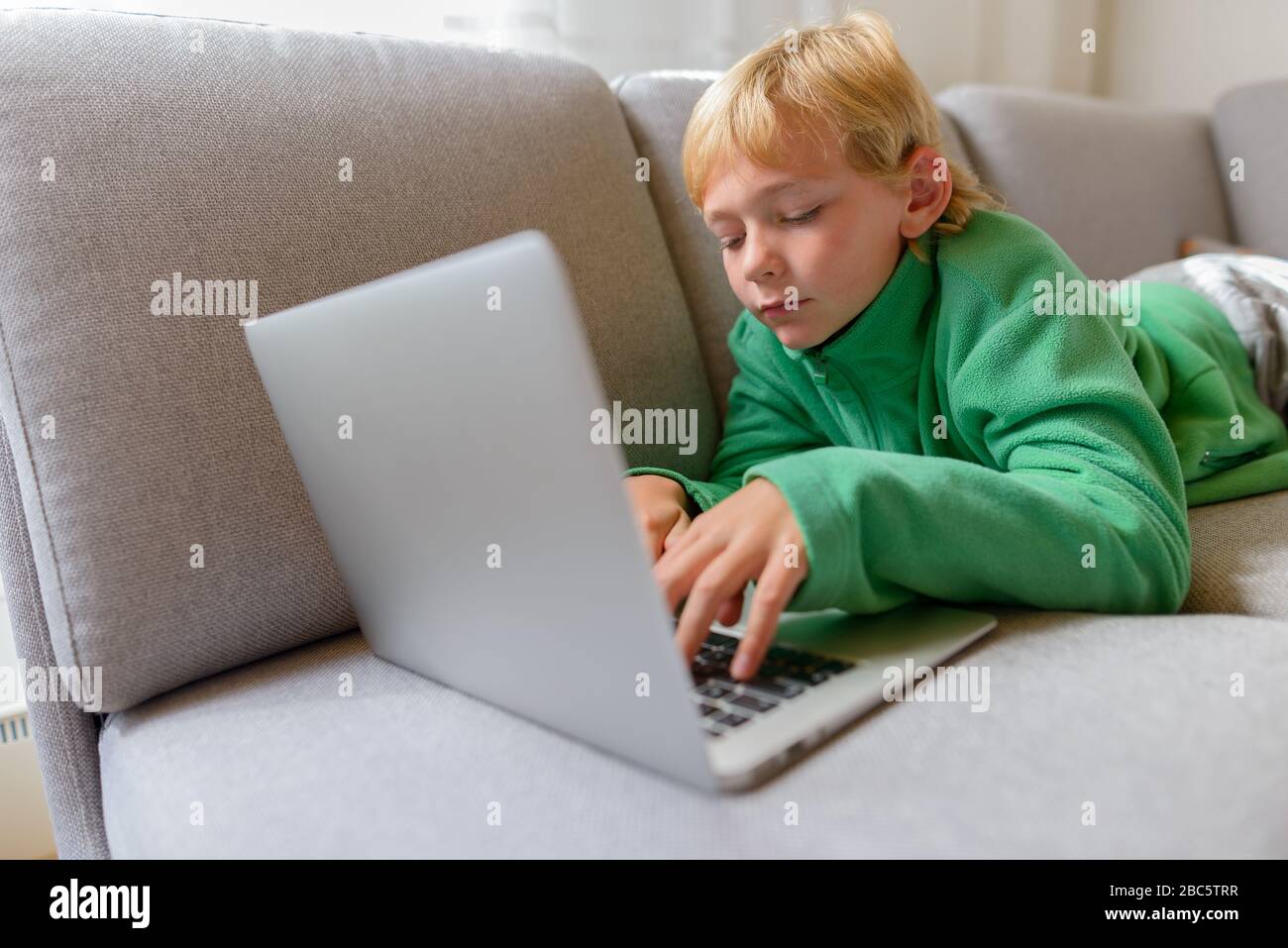 Jeune beau garçon allongé tout en utilisant l'ordinateur portable sur le canapé à la maison Banque D'Images
