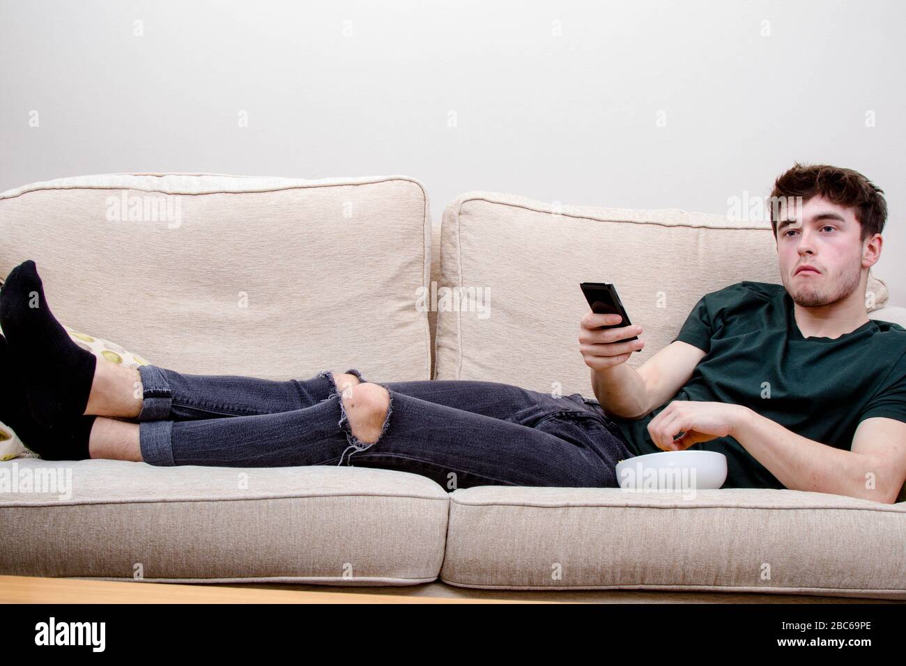 Un jeune homme adulte s'allongeant sur un canapé regardant la télévision et mangeant des en-cas Banque D'Images