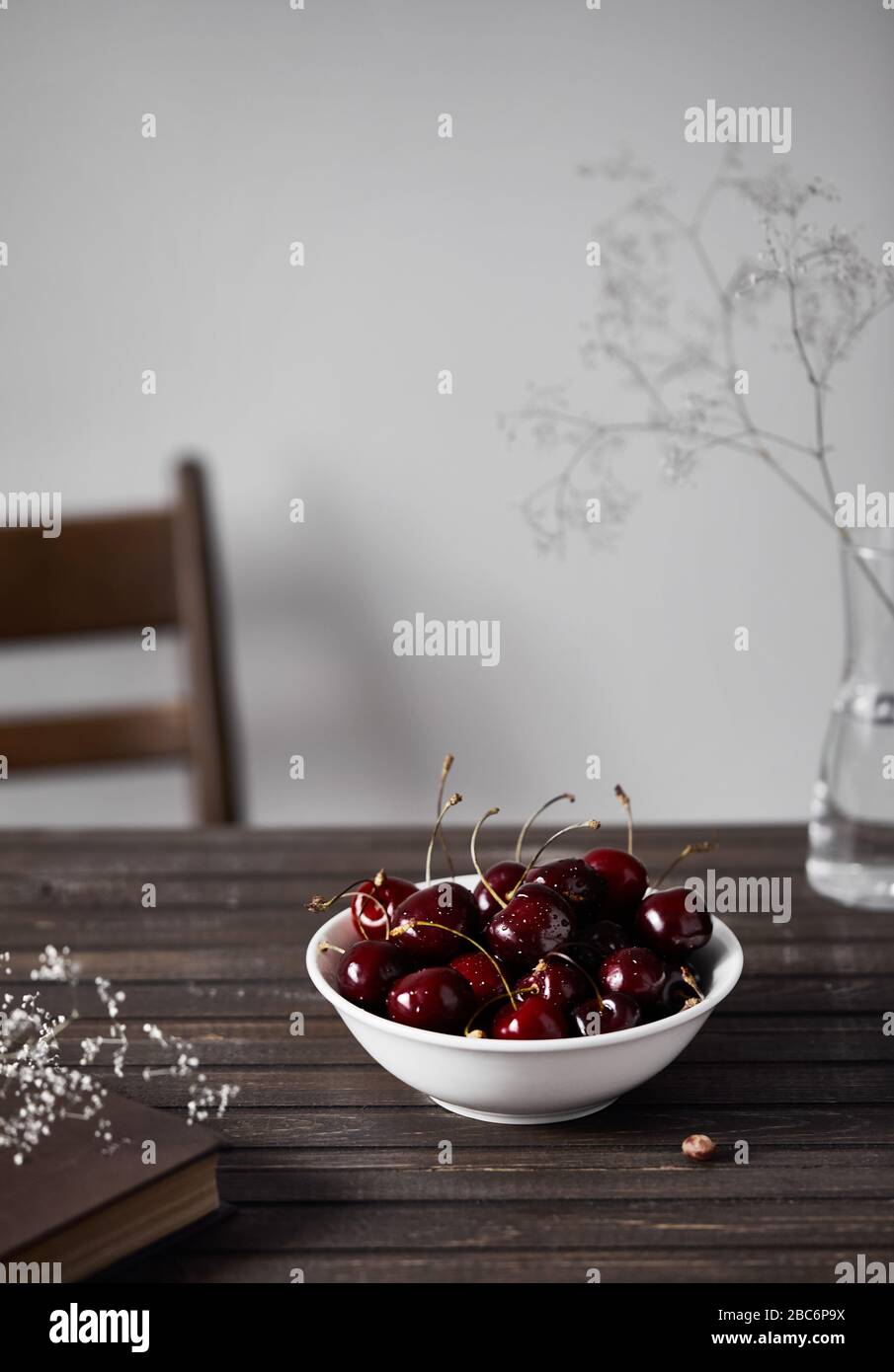 Cerise noire dans le bol blanc sur la table en bois près des fleurs blanches et réserver sur fond blanc en été Banque D'Images