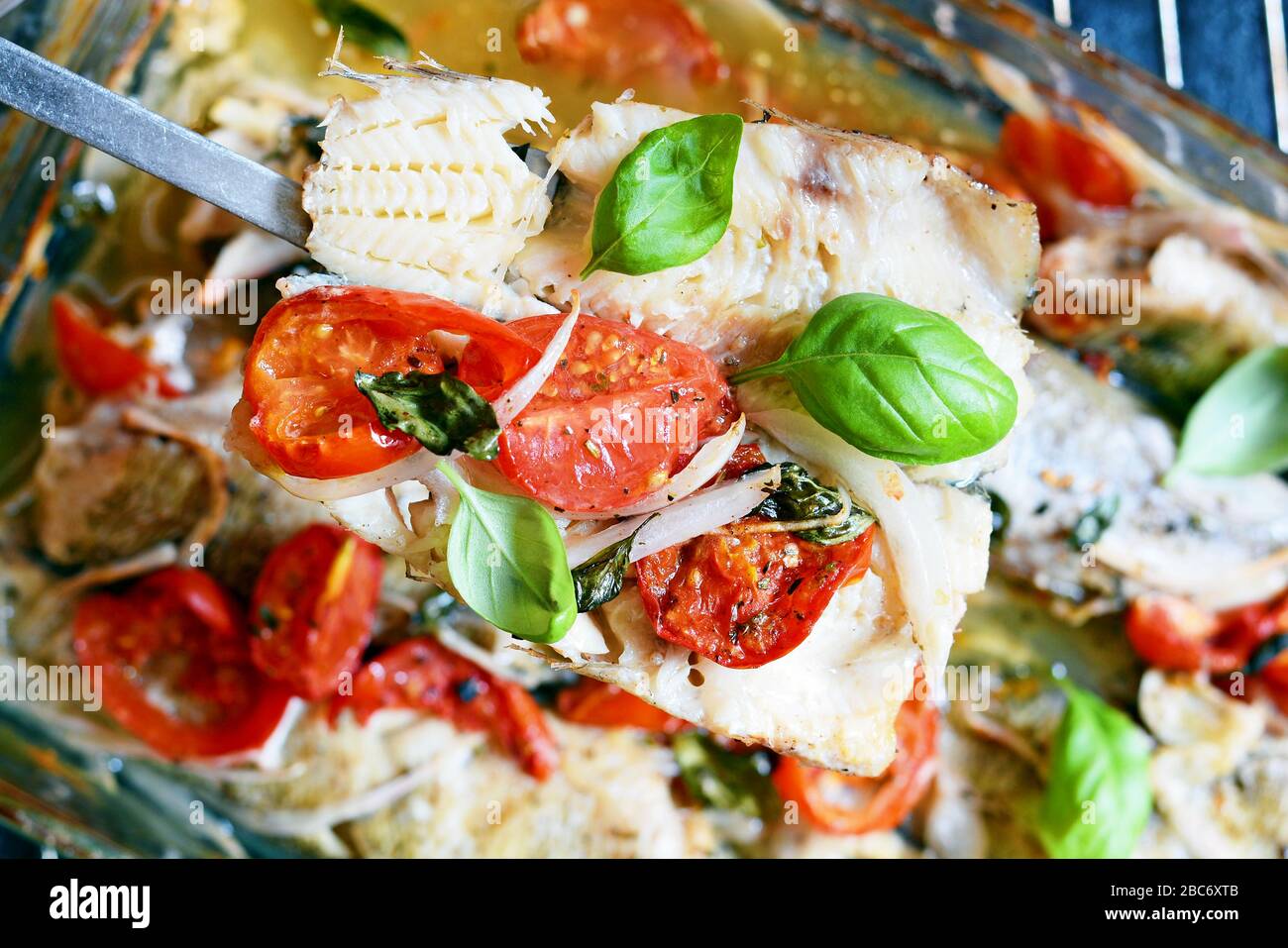 Poisson blanc (pollock, morue, merlu) cuit avec tomates, herbes italiennes et feuilles de basilic frais dans leur propre jus. Délicieux fruits de mer méditerranéens Banque D'Images
