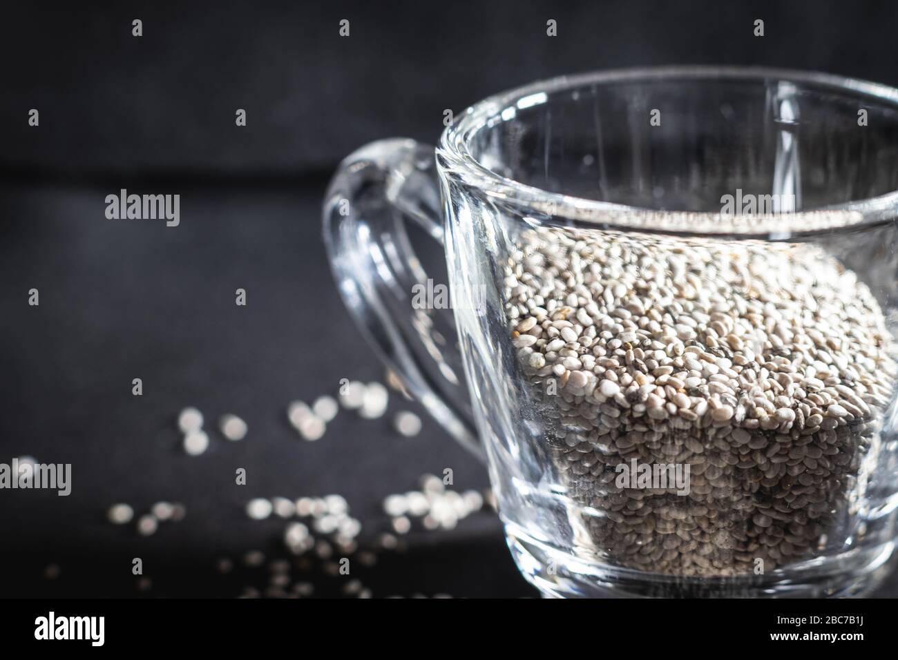 Gros plan de graines de chia blanc biologique, dans un petit mug en verre sur fond noir Banque D'Images