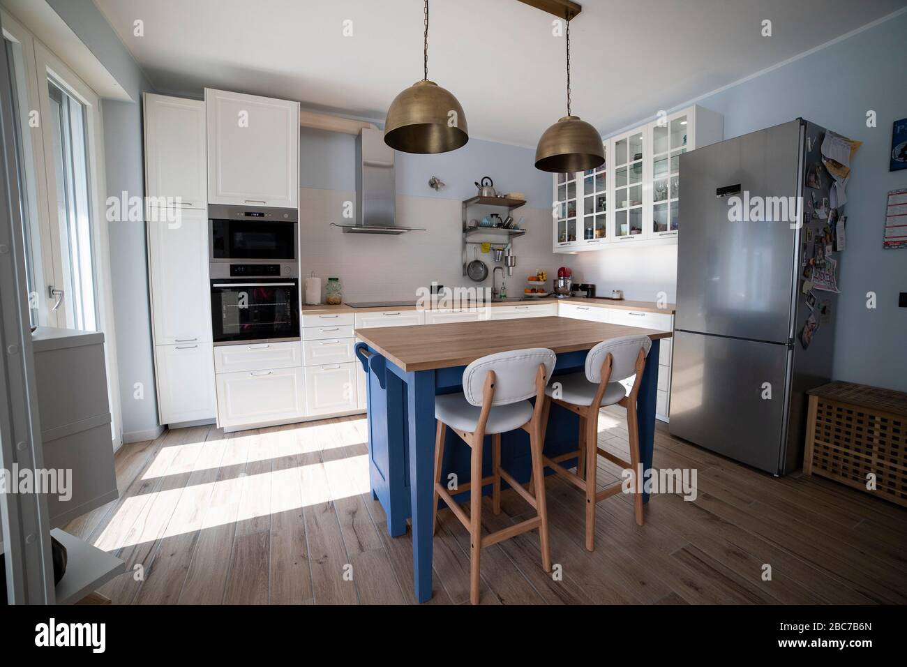 Cuisine blanche, lumineuse et scandinave avec îlot bleu et deux lampes suspendues en laiton. Banque D'Images