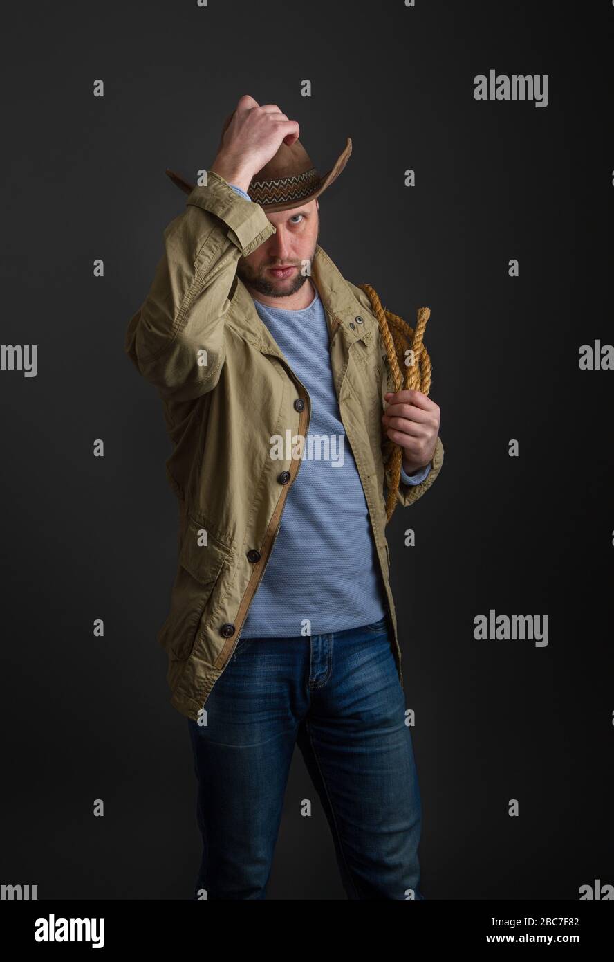 Cowboy dans un chapeau et une veste à large bord avec un lasso sur son  épaule se posant sur un fond sombre Photo Stock - Alamy