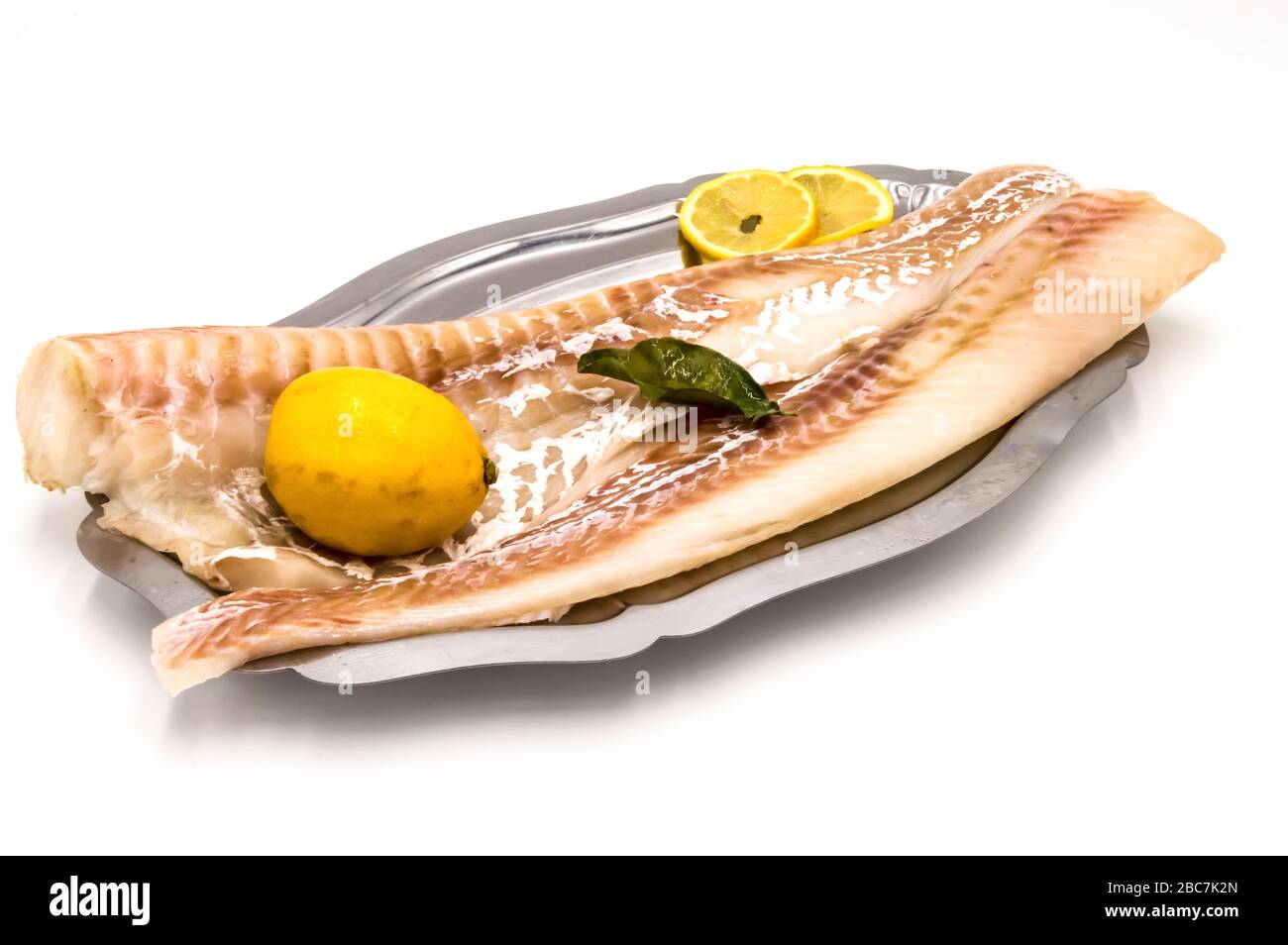 Filets de morue sur un plat en acier inoxydable avec un citron sur fond blanc Banque D'Images Filets de morue sur un plat en acier inoxydable avec un citron sur fond blanc Banque D'Images