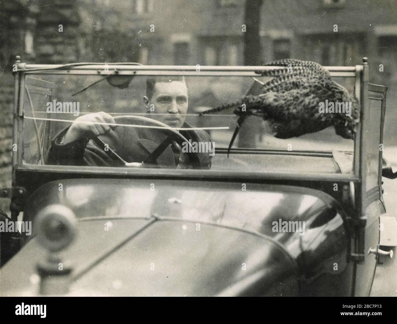 Un automobiliste assis à la roue de sa voiture montrant le pare-brise percé et le Pheasant, Nottingham, Royaume-Uni 1930 Banque D'Images