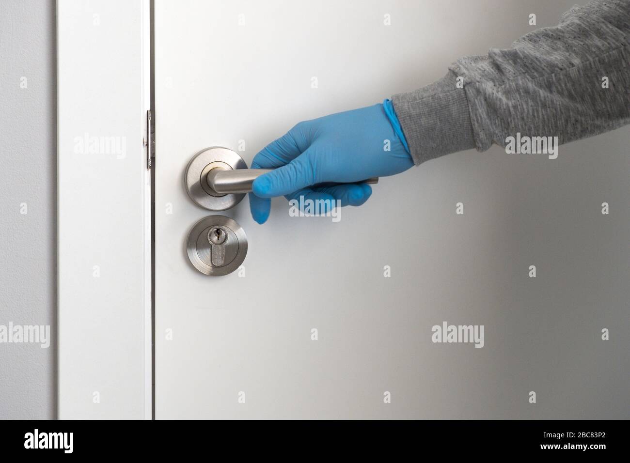 Une main dans un gant de protection bleu tient un pommeau de porte et est sur le point d'ouvrir la porte. Concept de santé et de protection. Banque D'Images