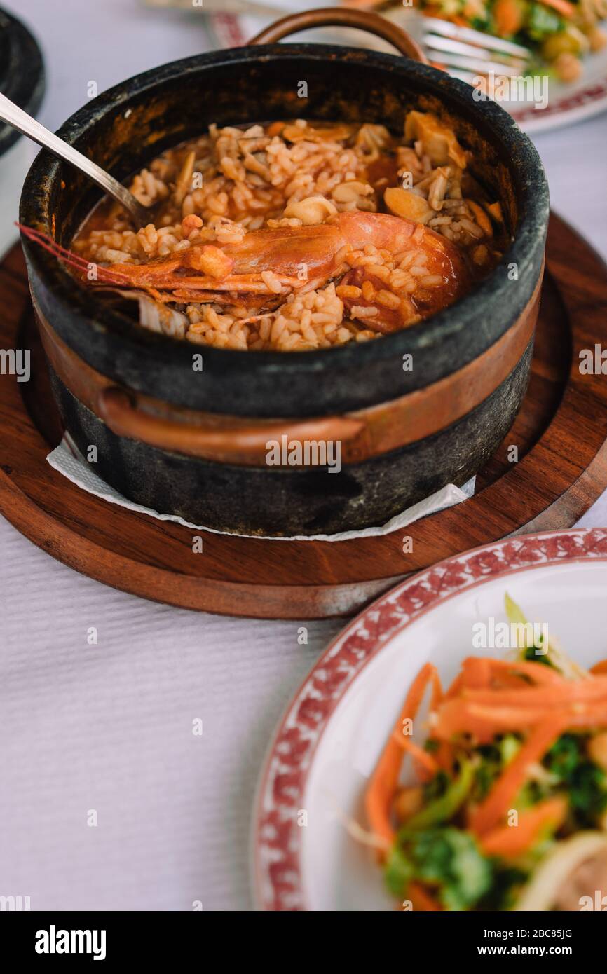 La cuisine nationale du Cap-Vert : Cachupa avec crevette nordique dans un bol traditionnel en pierre avec une salade de légumes sur une assiette. Banque D'Images