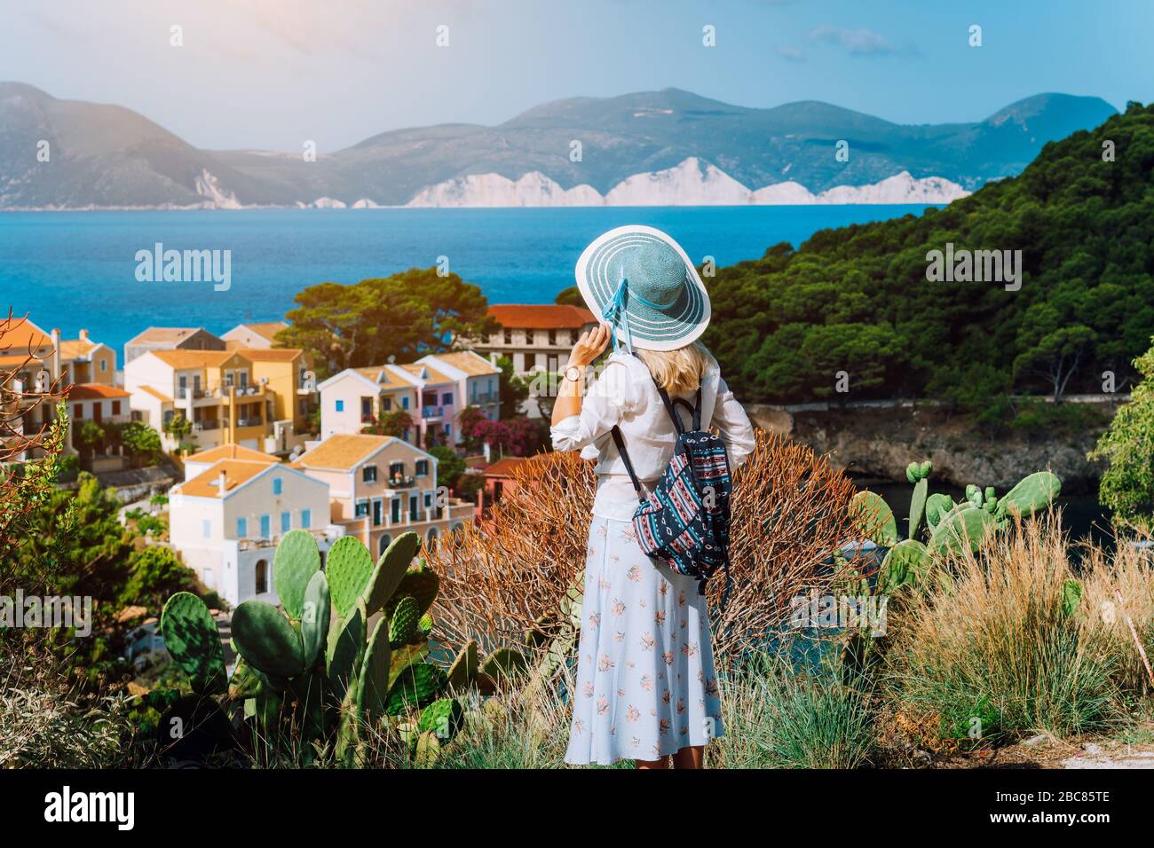 Photo vintage de la touriste féminine portant un chapeau bleu de soleil et un sac à dos de voyage profitant de la côte grecque dans la petite ville d'Assos. Kefalonia, Grèce. Banque D'Images