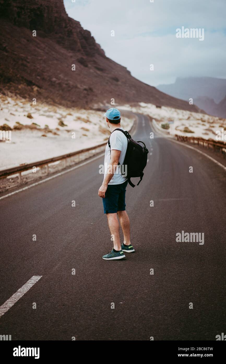 Voyageur avec sac à dos debout au centre d'une route épique sinueuse. D'énormes montagnes volcaniques à la distance derrière lui. Sao Vicente Cap-Vert. Banque D'Images