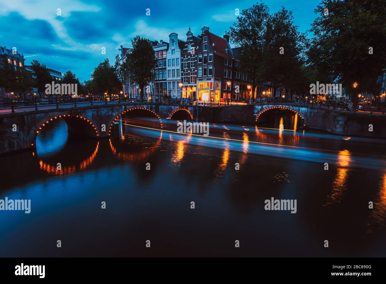 L'éclairage du pont et les sentiers légers du bateau en soirée Amsterdam avec réflexion sur le canal Herengracht. Maisons typiquement hollandaises à la lumière du crépuscule, Hollande, Neth Banque D'Images