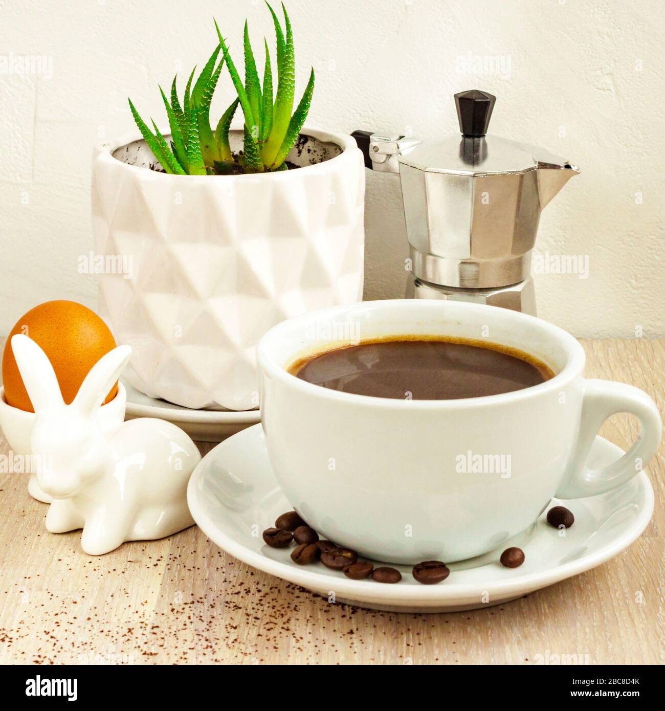 Tasse à café, soucoupe, haricots, cafetière en aluminium, plante succulente en pot, porte-œufs de lapin de Pâques Banque D'Images