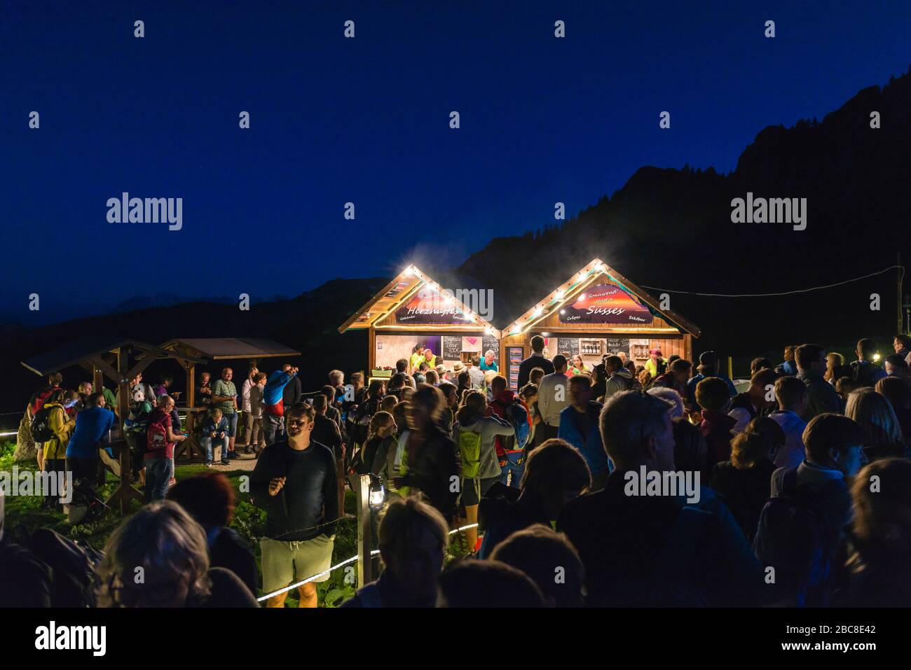 Les visiteurs se tiennent en ligne devant deux stands illuminés d'en-cas pendant le feu du milieu de l'été, Kampenwand, Chiemgau, Bavière, Allemagne, Europe Banque D'Images