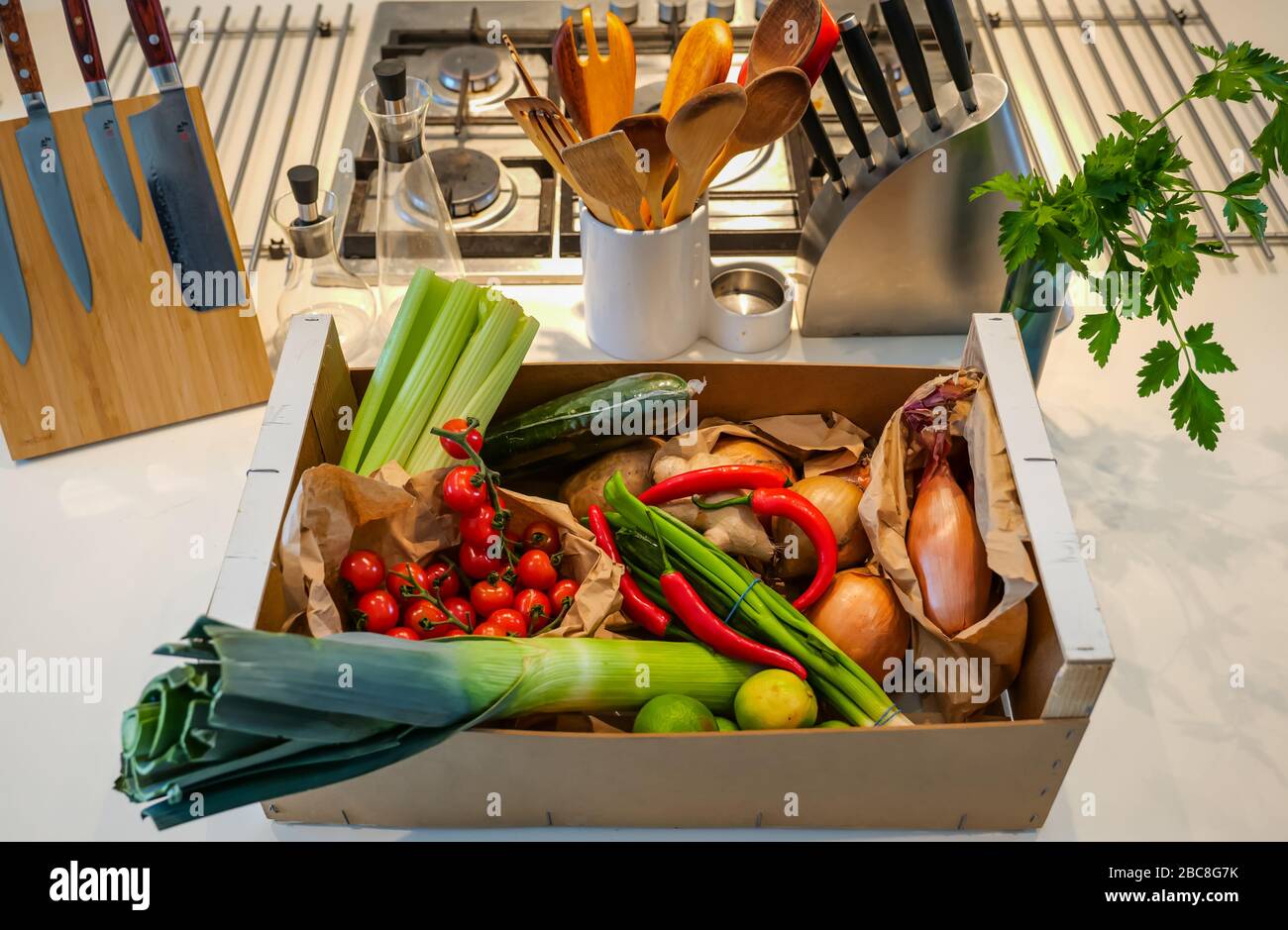 Livraison locale de légumes frais sur le comptoir de cuisine: Céleri, tomates cerises, poireaux, oignons, pommes de terre, chilis rouges, oignons de printemps et limes Banque D'Images