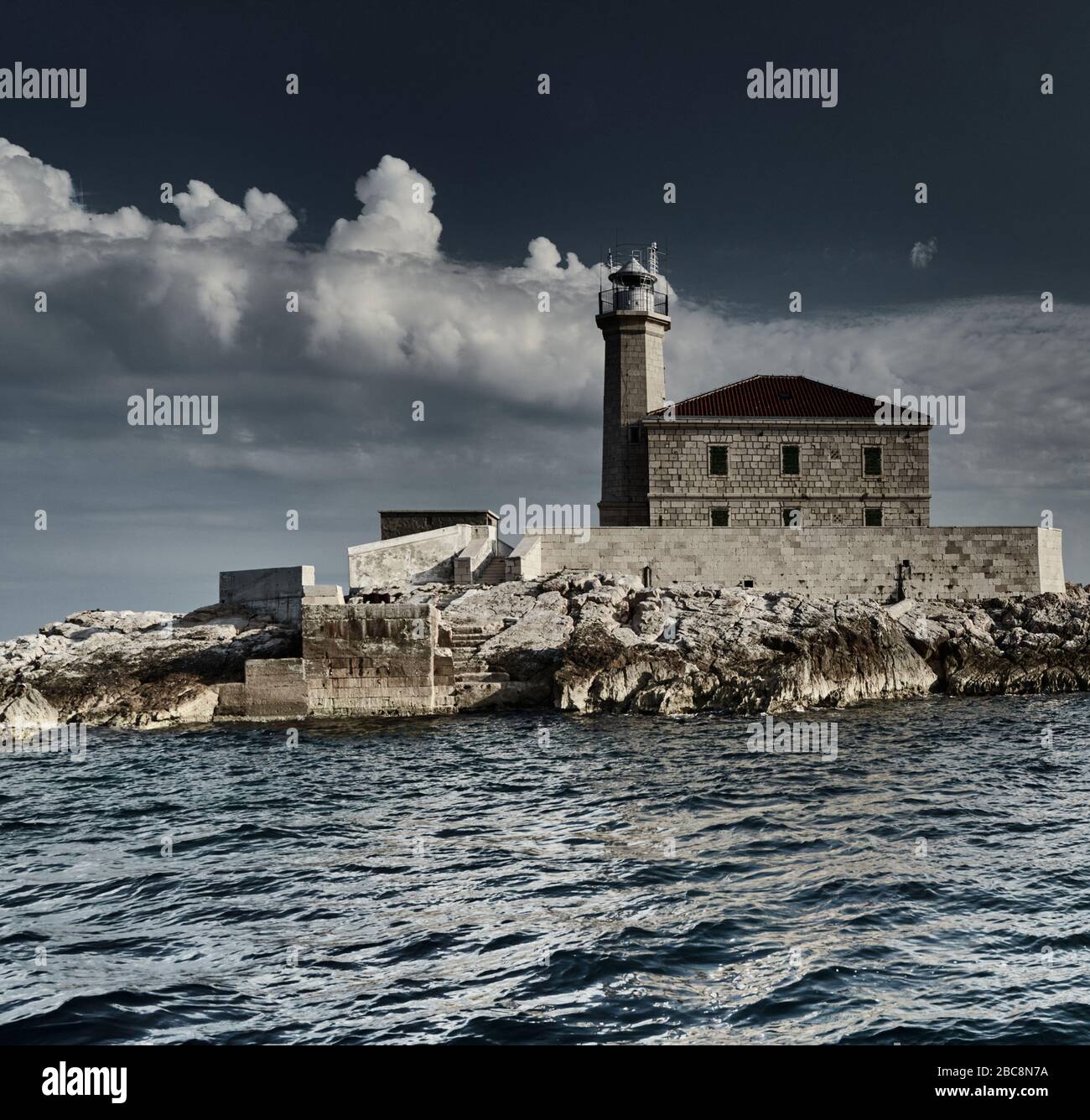 L'île avec un phare en Espagne au coucher du soleil, de grands nuages blancs sont en arrière-plan, la réflexion est sur l'eau Banque D'Images