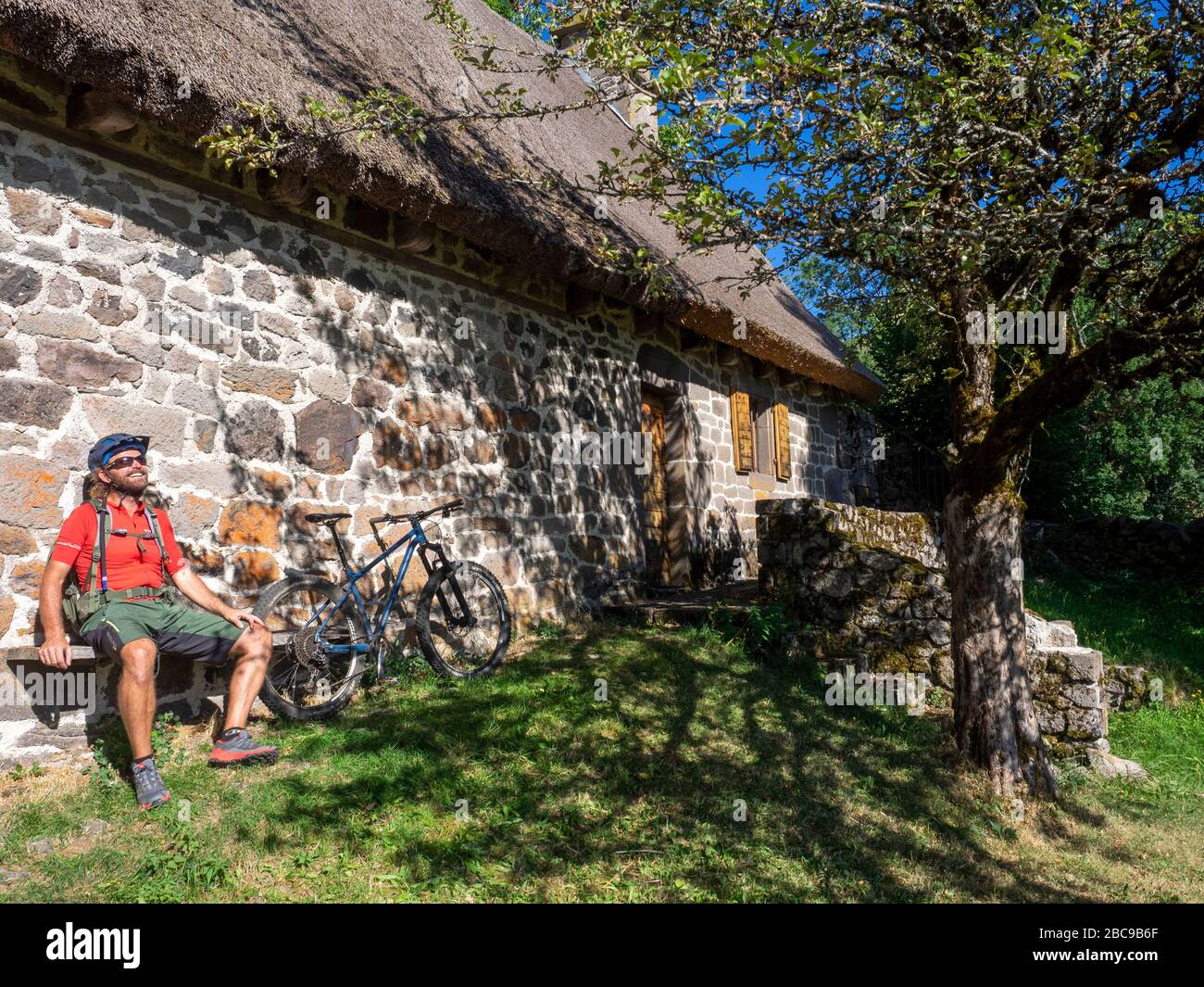 Les cyclistes de montagne reposent sur un banc en bois d'une ancienne ferme de montagne, Chaumière de Granier à Nierveze, Thiézac. Monts du Cantal, Massif Central, Cantal FRA Banque D'Images