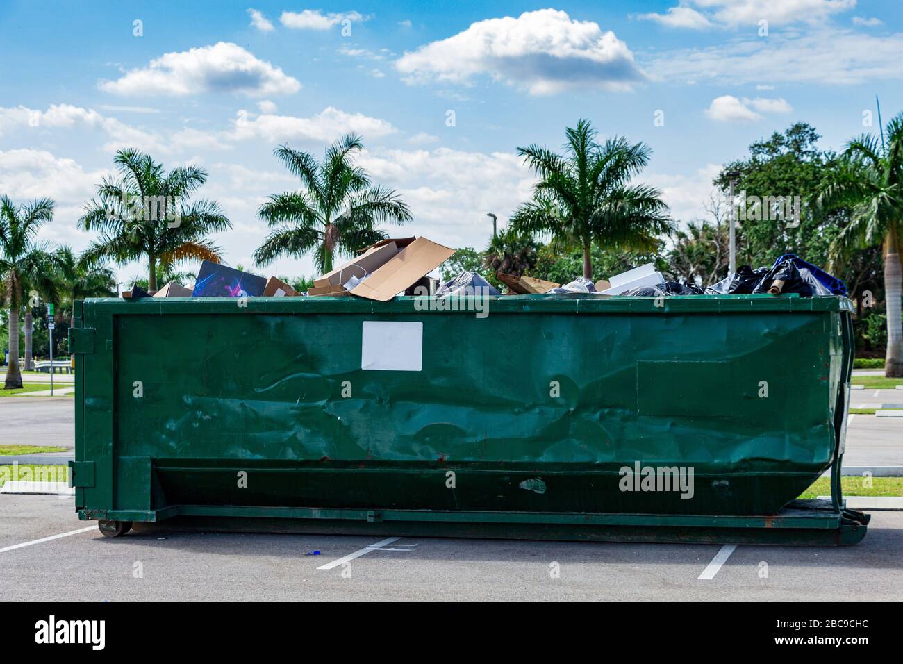 Grand dépotoir en métal vert rempli de déchets dans le parking - Davie, Floride, États-Unis Banque D'Images