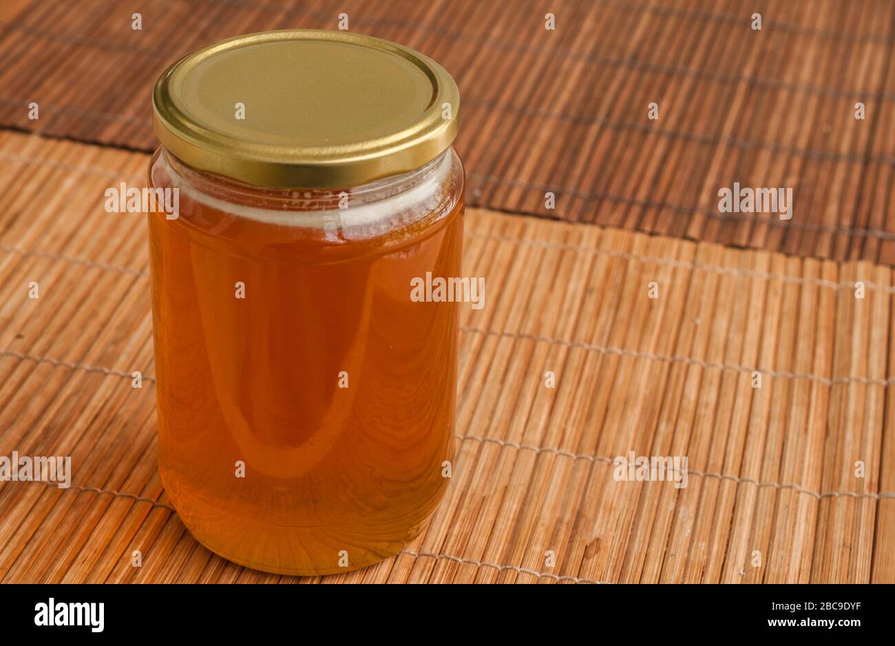 Bocal en verre plein de miel d'abeille se ferme sur le tapis Reed Banque D'Images