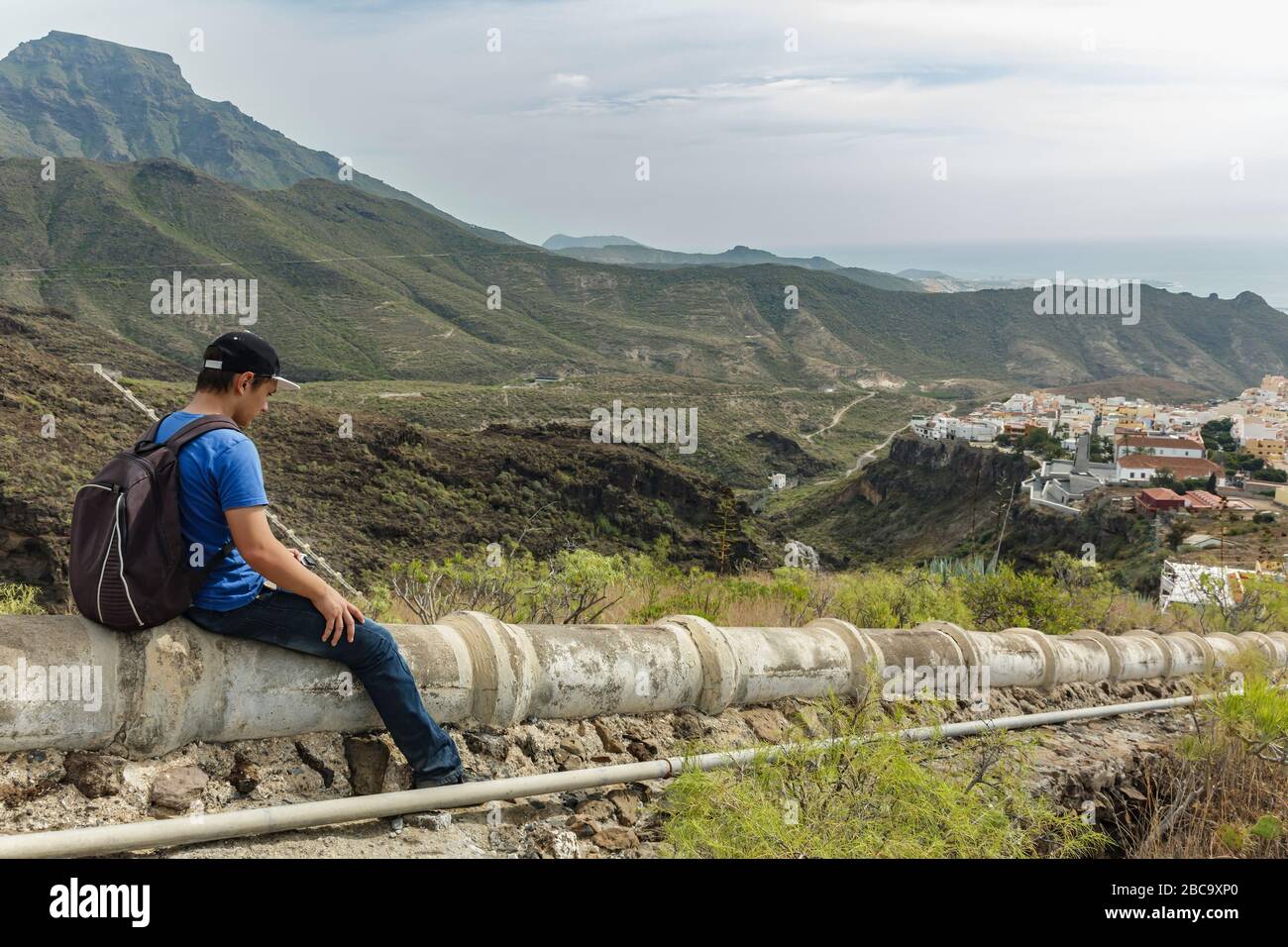 Un jeune homme avec un sac à dos sur l'aqueduc en béton dans le côté ouest de Tenerife près du village d'Adeje. Randonnée pédestre par le sentier de montagne Banque D'Images