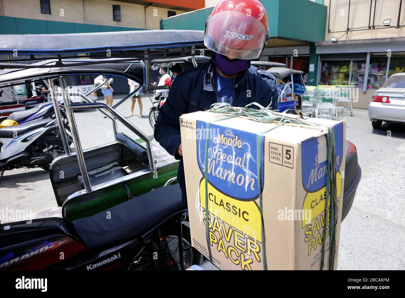 Antipolo City, Philippines - 2 avril 2020: L'homme charge une grande boîte remplie d'articles d'épicerie qu'il vient d'acheter sur sa moto pendant le verrouillage ou le trajet Banque D'Images