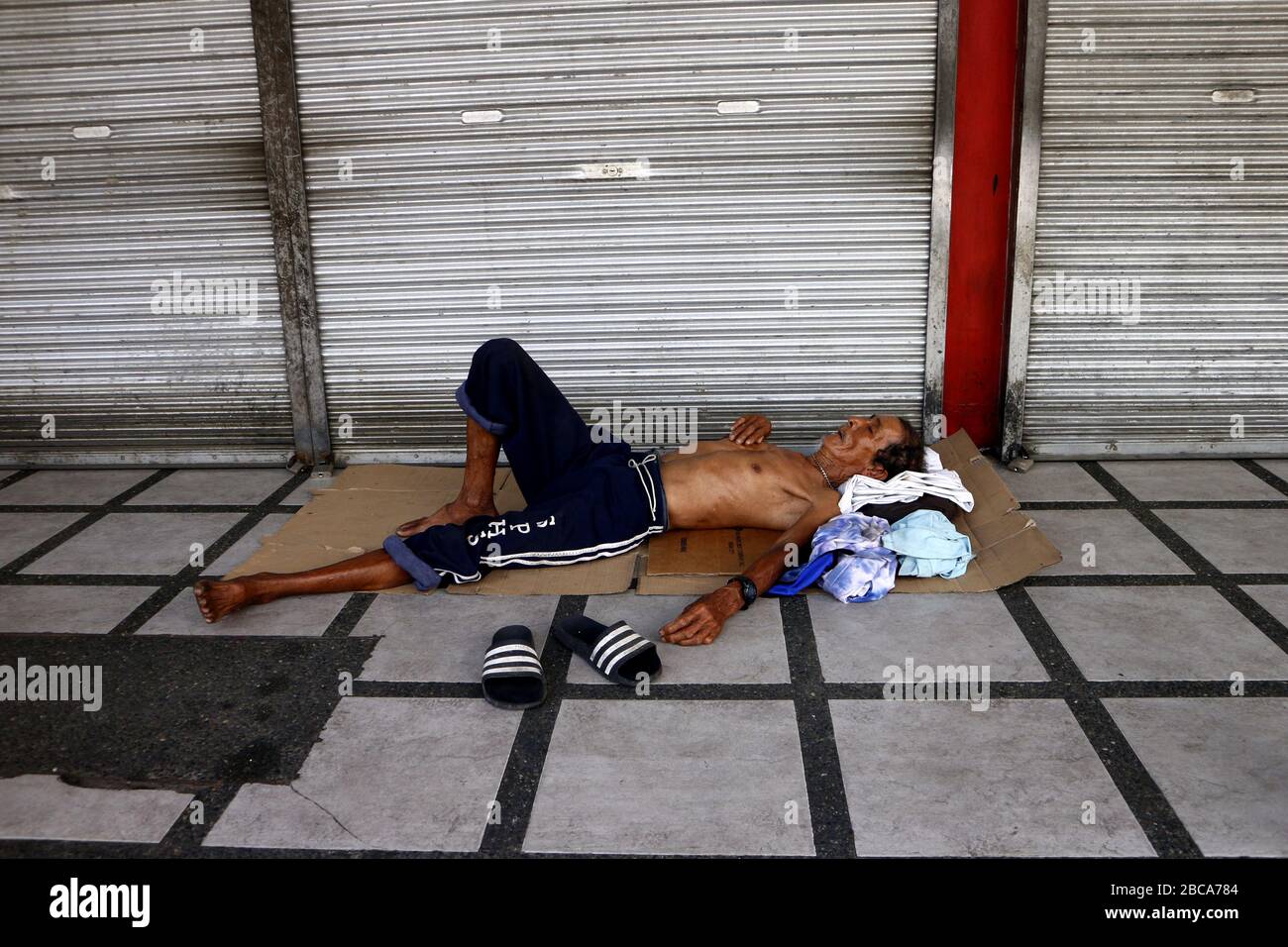 Antipolo City, Philippines - 2 avril 2020: Un homme sans abri philippin dort sur le sidwalk devant un magasin fermé pendant le verrouillage ou la communauté qu Banque D'Images