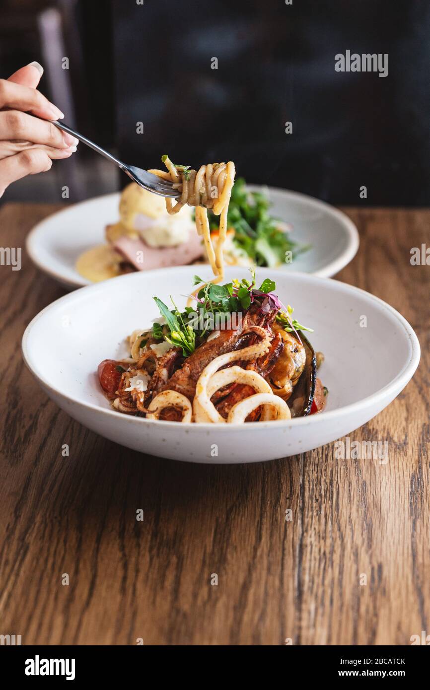 Pincer les fruits de mer Spaghetti à la main et lever avec une fourchette : spaghetti aux crevettes, calmars, moules cuites à l'huile d'olive, chilis et ail. Banque D'Images