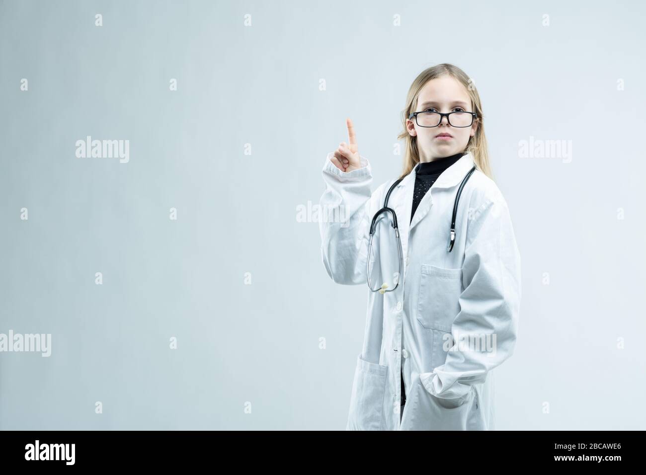 Petite fille amusante portant des lunettes habillées comme médecin ou infirmière dans un manteau blanc de laboratoire avec stéthoscope sur un fond blanc avec espace de copie Banque D'Images