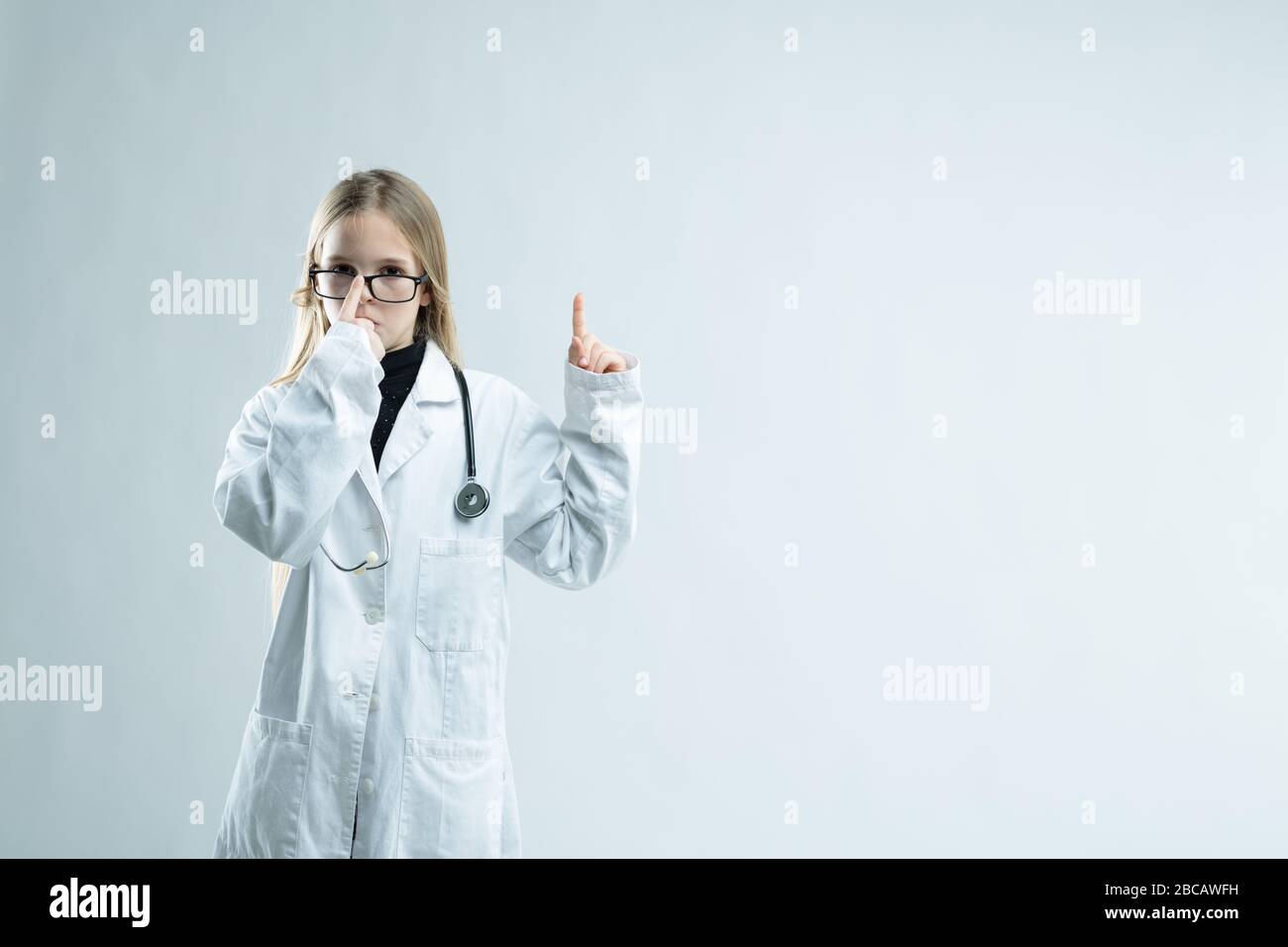 Jeune fille jouant à être médecin en blouse de laboratoire blanche, stéthoscope et lunettes de taille isolée sur blanc avec espace de copie Banque D'Images
