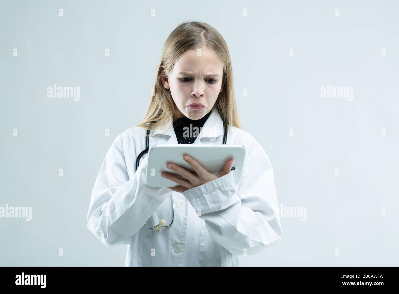 Jeune fille en laboratoire blanc manteau calmant à un presse-papiers avec une expression morose comme elle prétend être un médecin ou une infirmière isolée sur blanc Banque D'Images