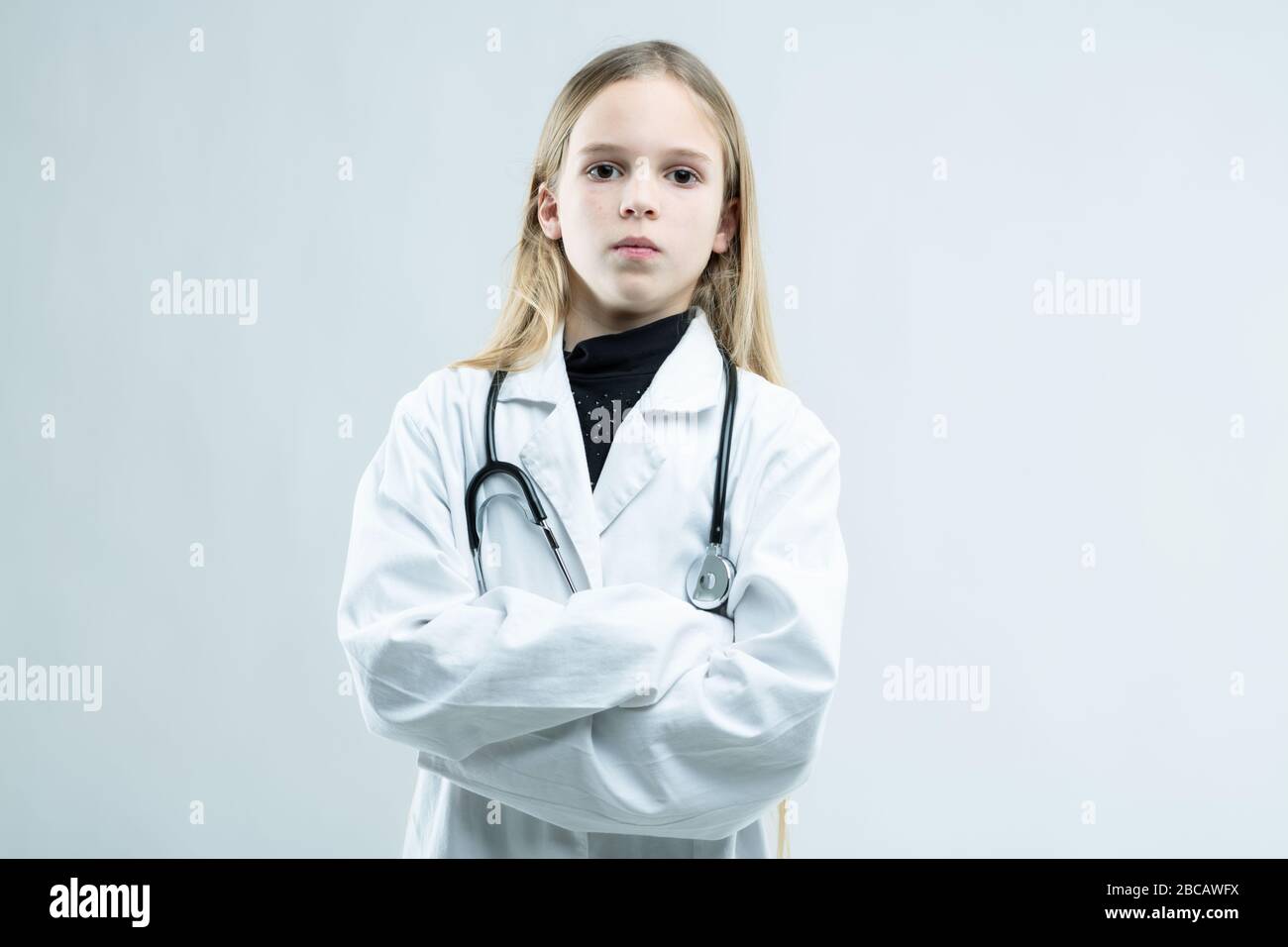 Jeune fille blonde vêtue comme médecin ou infirmière réalisant son rêve d'enfance debout avec des bras repliés affamant à la caméra isolée sur blanc avec cop Banque D'Images