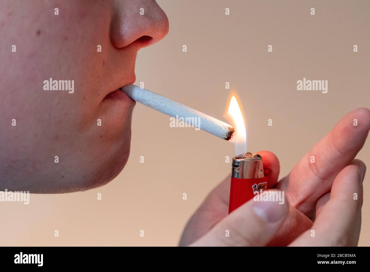 L'homme allume le joint de marijuana avec un briquet rouge Bic. Banque D'Images